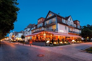 A hotel with a restaurant on the ground floor, featuring a cobblestone street and a clear evening sky.
