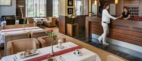 Un vestíbulo de hotel con mostrador de recepción, zona de estar y mesas dispuestas para comer.