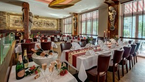 Een restaurant met meerdere eettafels, een bar met flessen en een groot decoratief kunstwerk aan de muur.