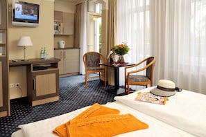 Ein Hotelzimmer mit Bett, Schreibtisch mit Computer, Stuhl, Fernseher und Fenster mit Vorhängen.