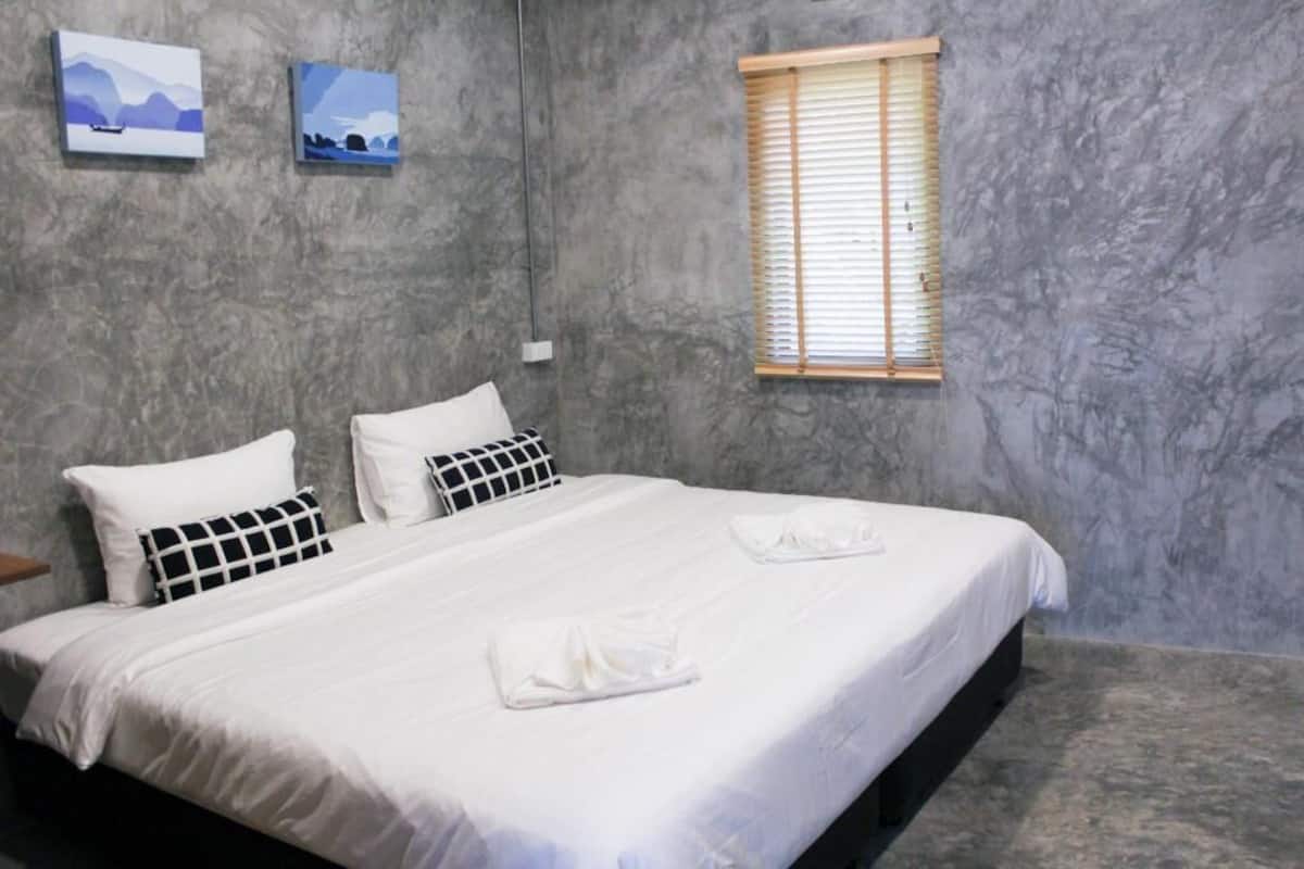 A bedroom with a bed, two pillows, a window with blinds, and two wall-mounted paintings.