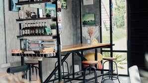 A cozy café with a wooden table, books, and bottles on shelves. - The Simple Koh Yao Noi (Ko Yao)