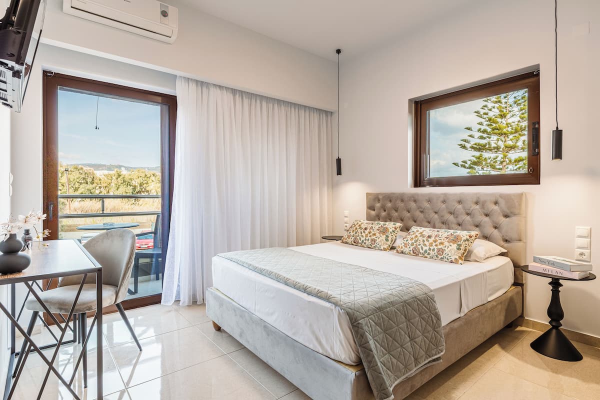 A bedroom with a bed, a dining table, chairs, a window with a view, and a bedside table with books.