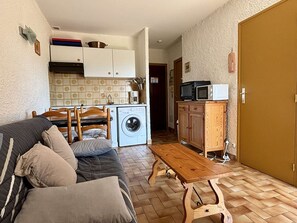 Ett kompakt bostadsutrymme med en soffa, ett träbord, en tvättmaskin och en mikrovågsugn.