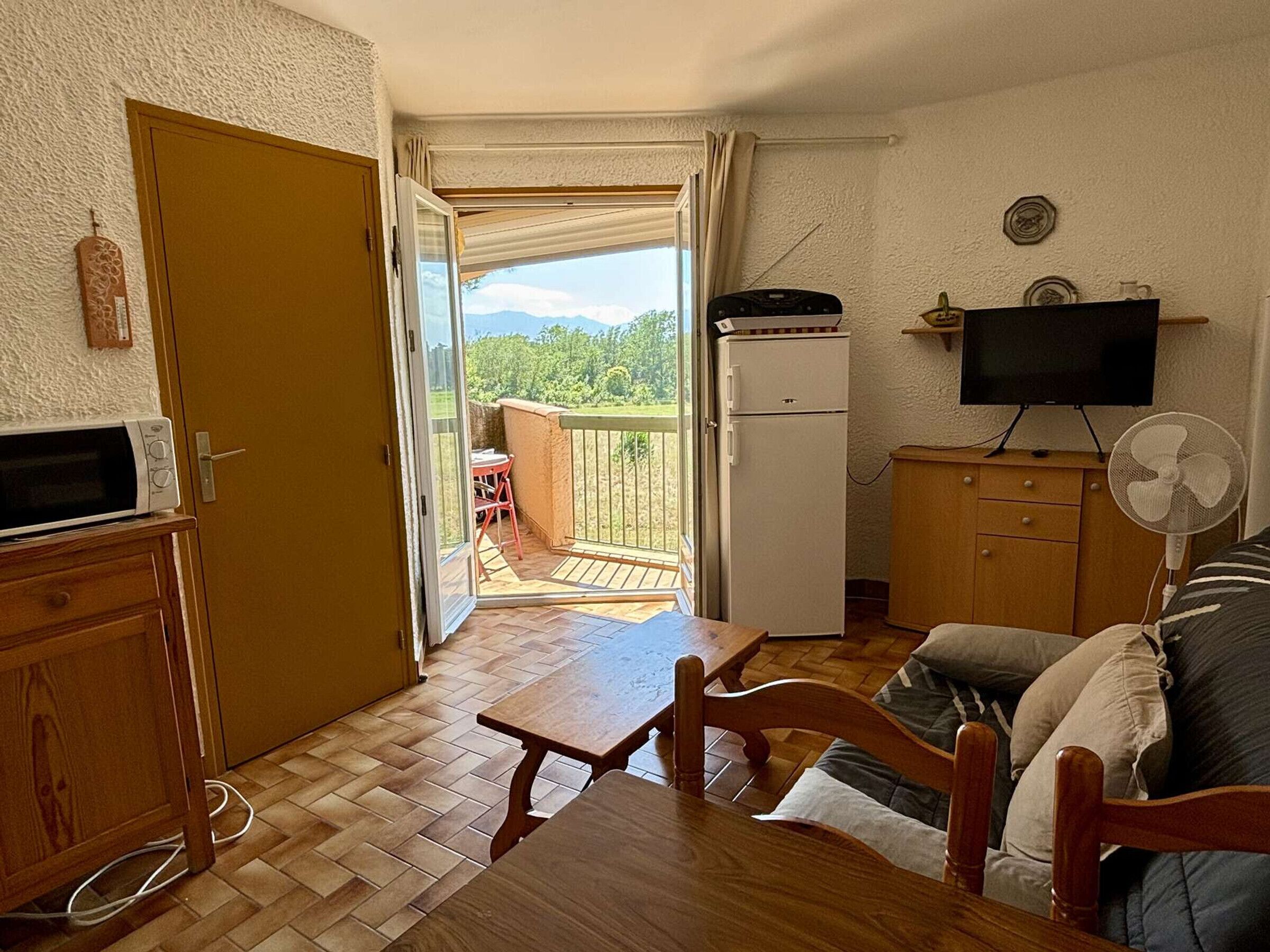 A small living area with a wooden table, a sofa, a TV, and a refrigerator.