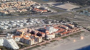Luchtbeeld van een kustgebied met een mix van woongebouwen en een groot hotelcomplex met meerdere verdiepingen en een centraal torentje.