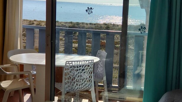 Een balkon met een tafel en stoelen, met uitzicht op een strand en een heldere horizon van de zee.