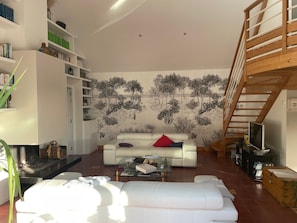 Un salon moderne avec un canapé blanc, une table basse en verre et une fresque représentant des arbres sur le mur.