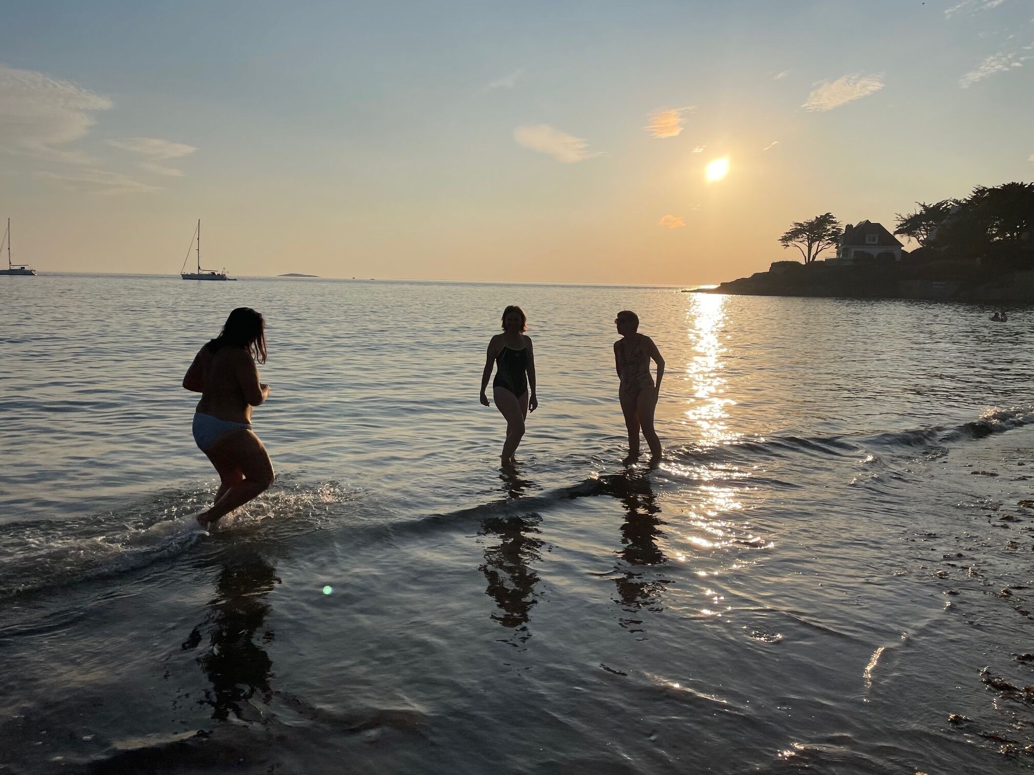 Trois personnes se promènent dans une eau peu profonde au coucher du soleil.