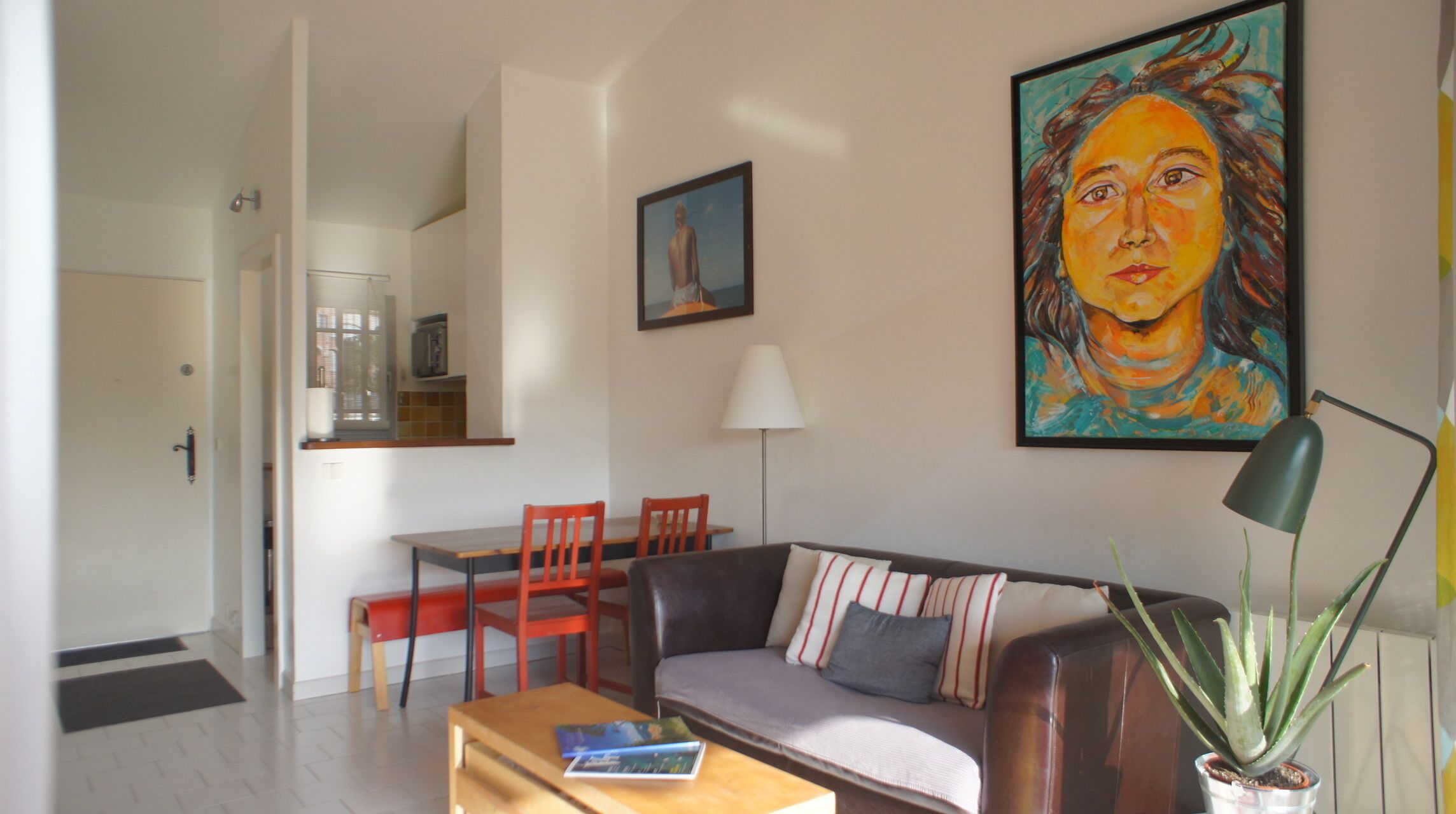 A living room with a sofa, a coffee table, a dining table with chairs, a painting, and a potted plant.