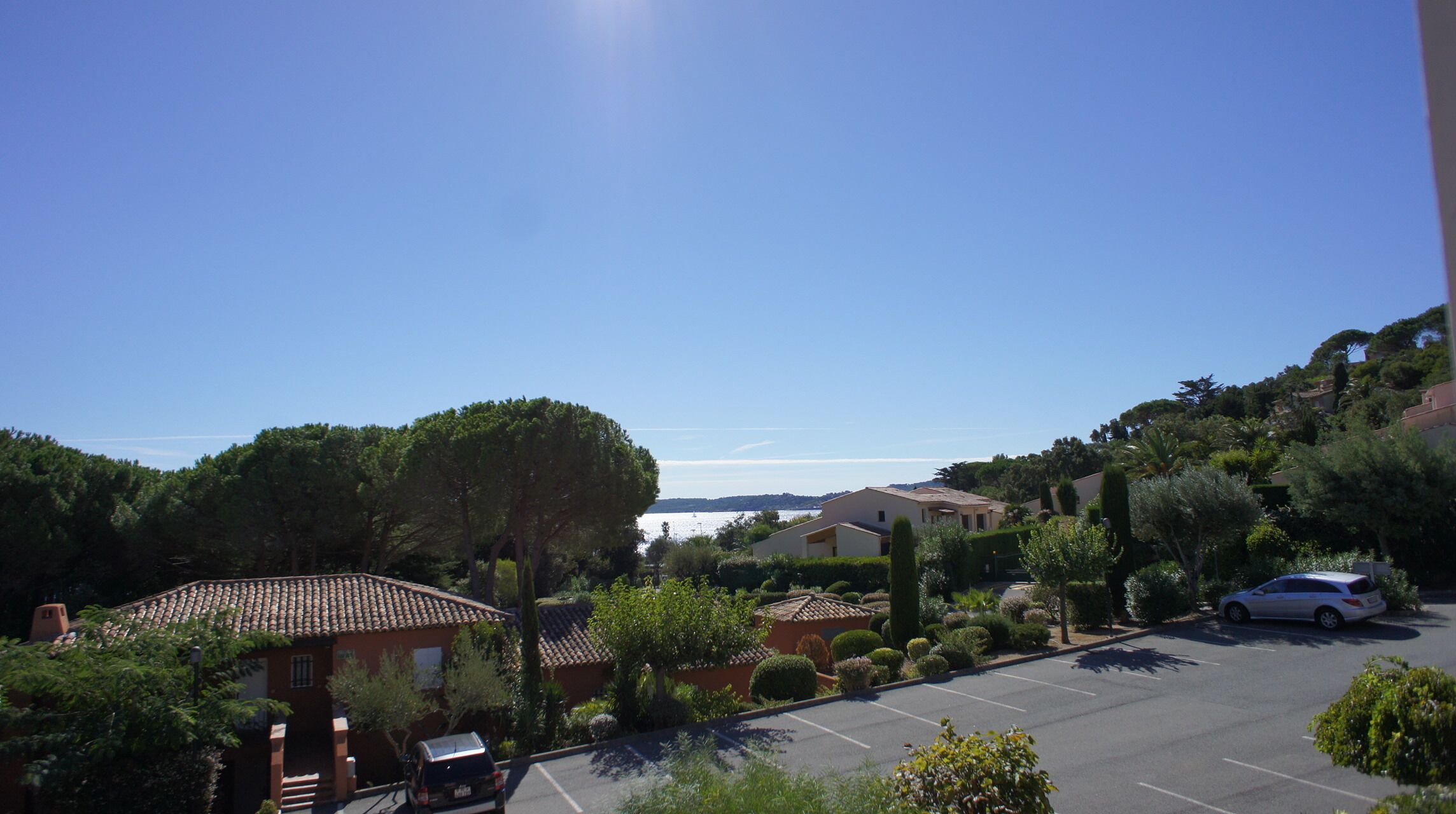 A residential area with a parking lot, houses with tiled roofs, and a clear view of the sea.