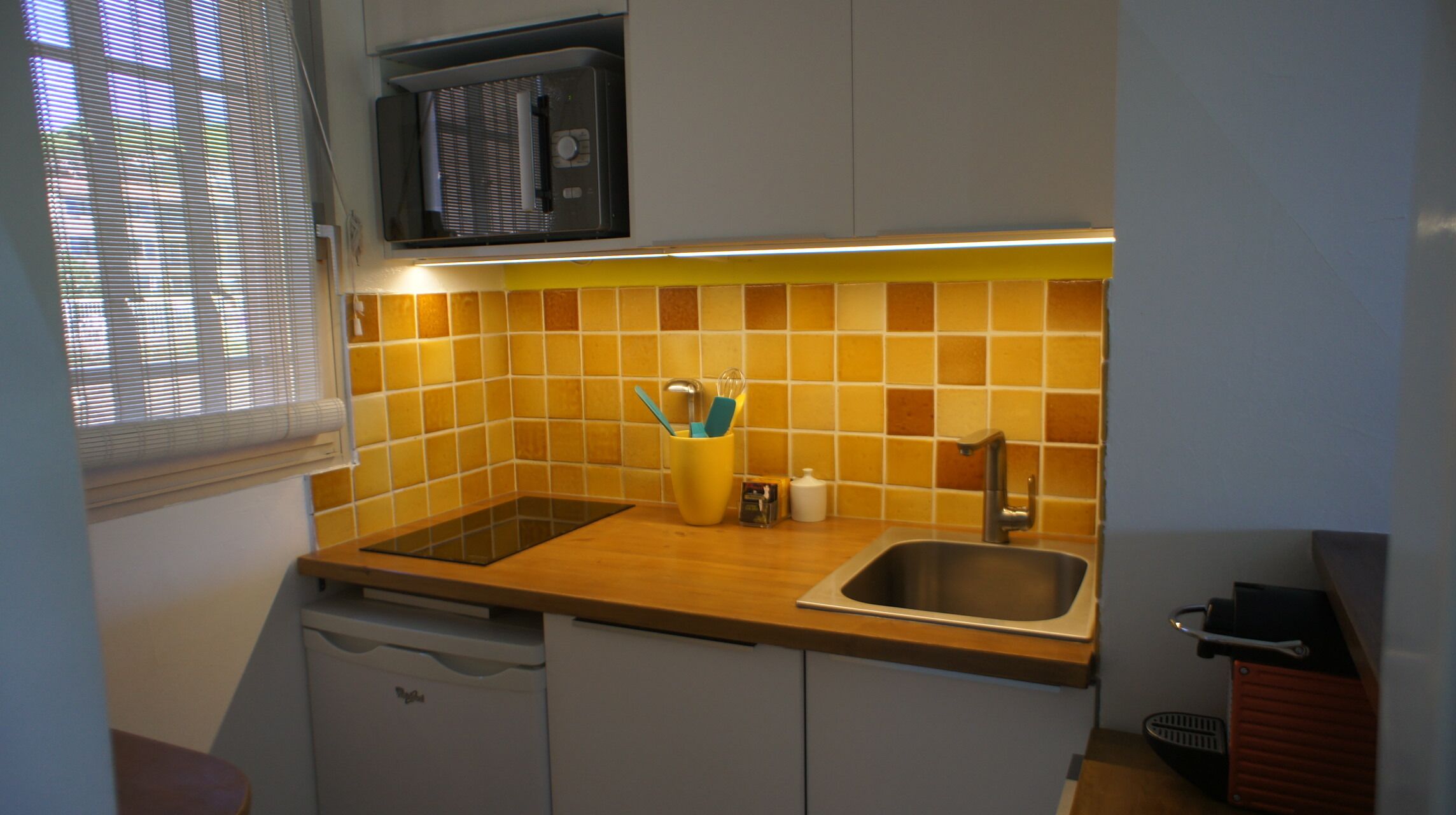 A compact kitchen with a microwave, sink, and a yellow-tiled backsplash.