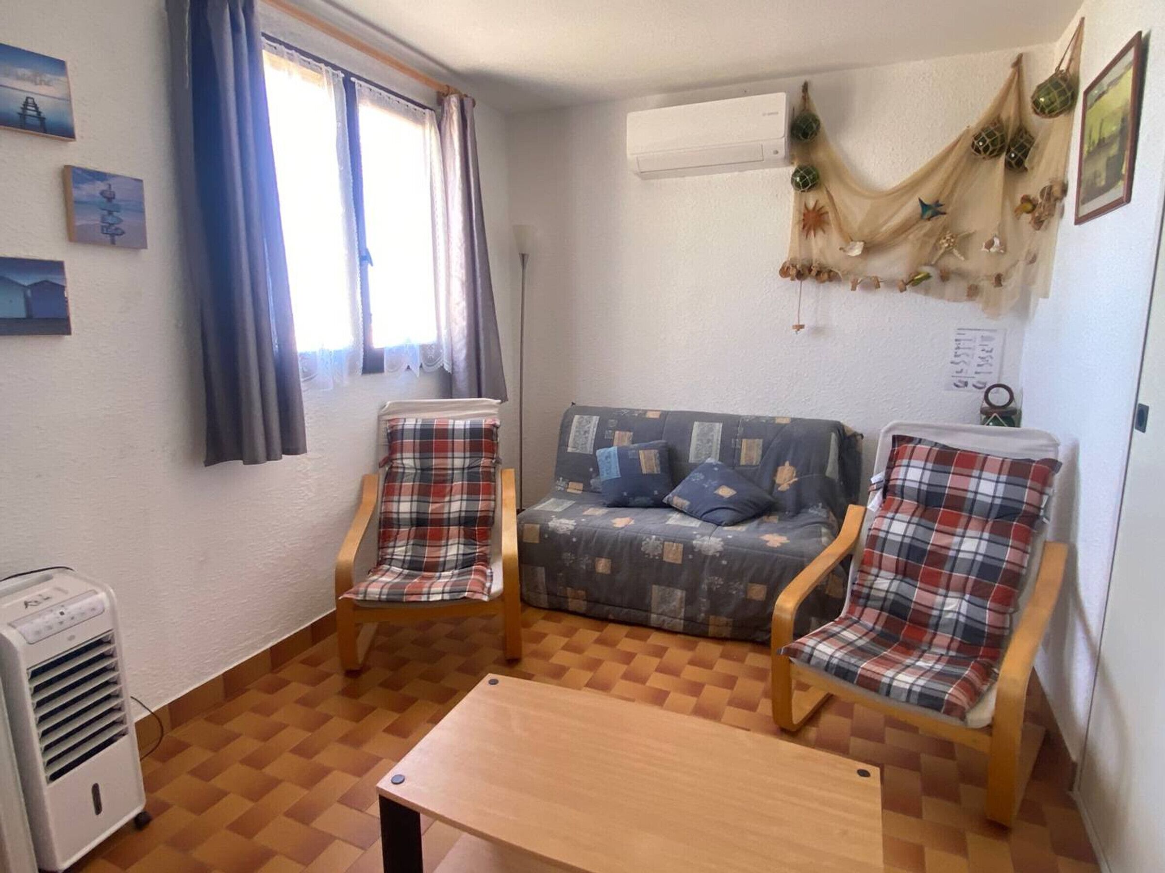 A small, cozy room with a sofa, two plaid chairs, a wooden table, and a window with curtains.
