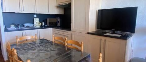 A compact kitchen with a dining table, chairs, a microwave, a coffee maker, and a television.