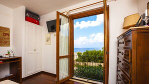 Una habitación con un aparador de madera, un escritorio con ordenador, un televisor en la pared y un balcón con vistas al mar.
