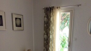 Una camera da letto con un letto, un comodino, una lampada, una finestra con tende e un condizionatore d'aria a muro.