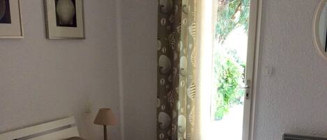 A bedroom with a bed, a nightstand, a lamp, a window with curtains, and a wall-mounted air conditioning unit.