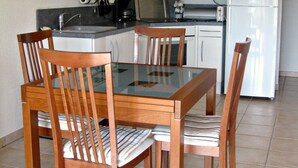 Una cucina compatta con mobili bianchi, un forno a microonde, un fornello e un frigorifero. C'è un tavolo da pranzo con quattro sedie.