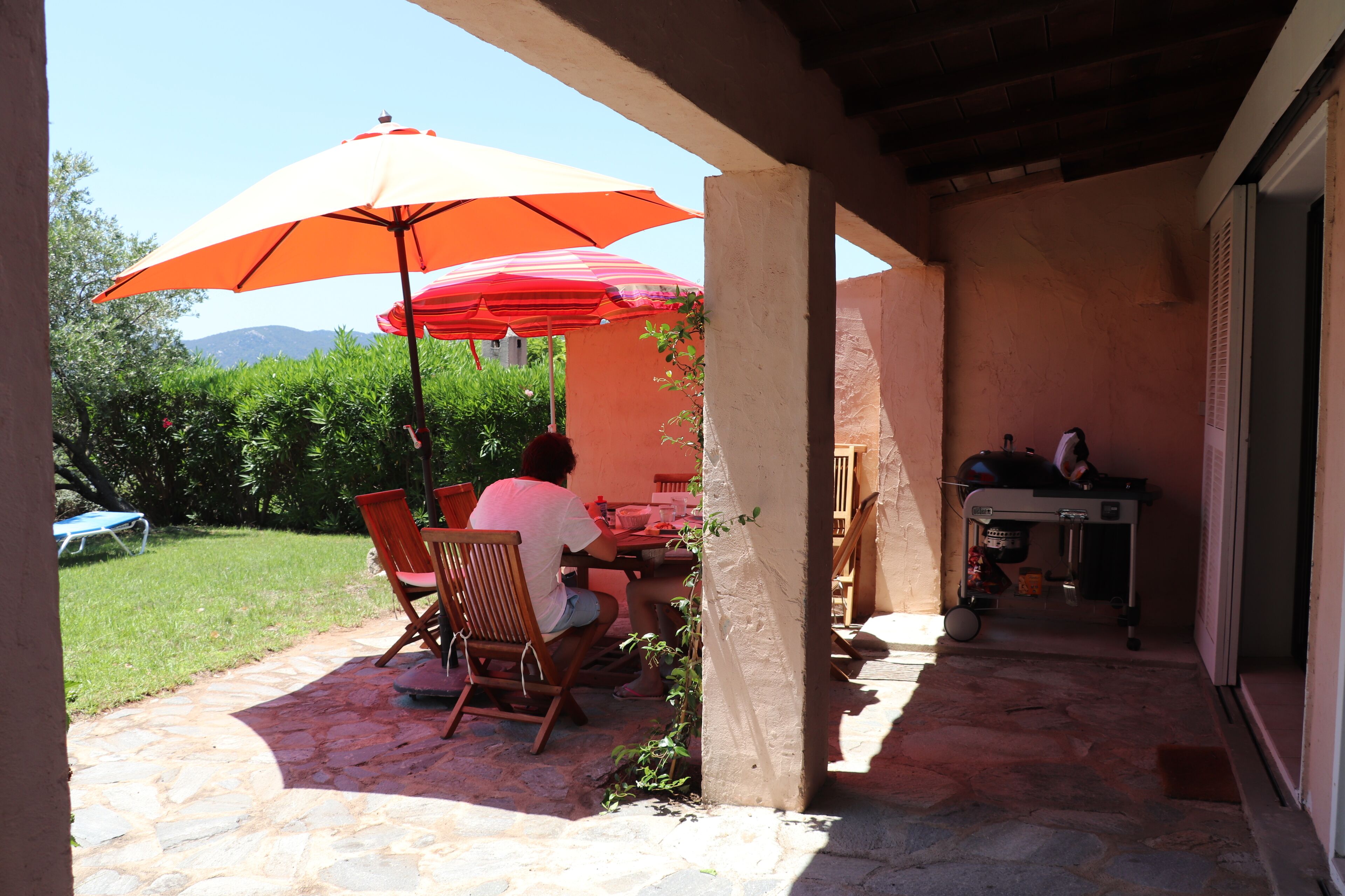 An outdoor patio with stone flooring, a table with chairs, and a large orange umbrella providing shade.