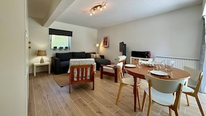 Un salon moderne comprenant un canapé, une table à manger avec des chaises, un téléviseur et un luminaire suspendu au plafond.