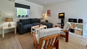 Un salon moderne avec un canapé, une chaise en bois, un téléviseur et une petite table.