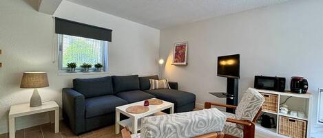 A modern living room with a sofa, a wooden chair, a TV, and a small table.