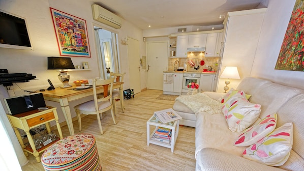 Een woonkamer met een bank, salontafel, televisie, bureau en een keukenhoek.