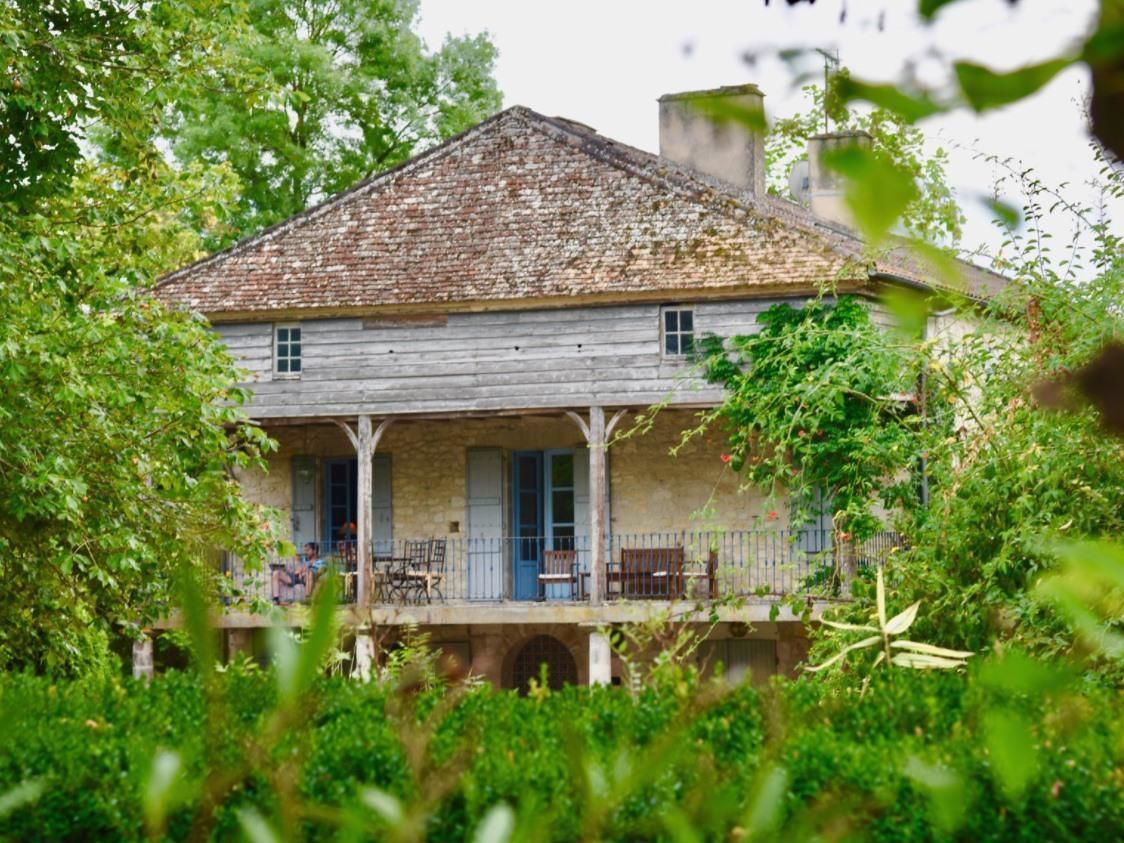 Une maison en bois à l’allure rustique, dotée d’un porche et entourée d’une végétation luxuriante.