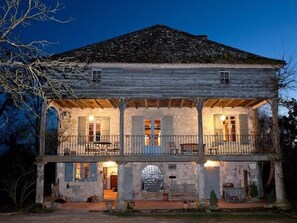 Una casa rústica de dos pisos con un balcón, paredes de piedra y techo de madera.