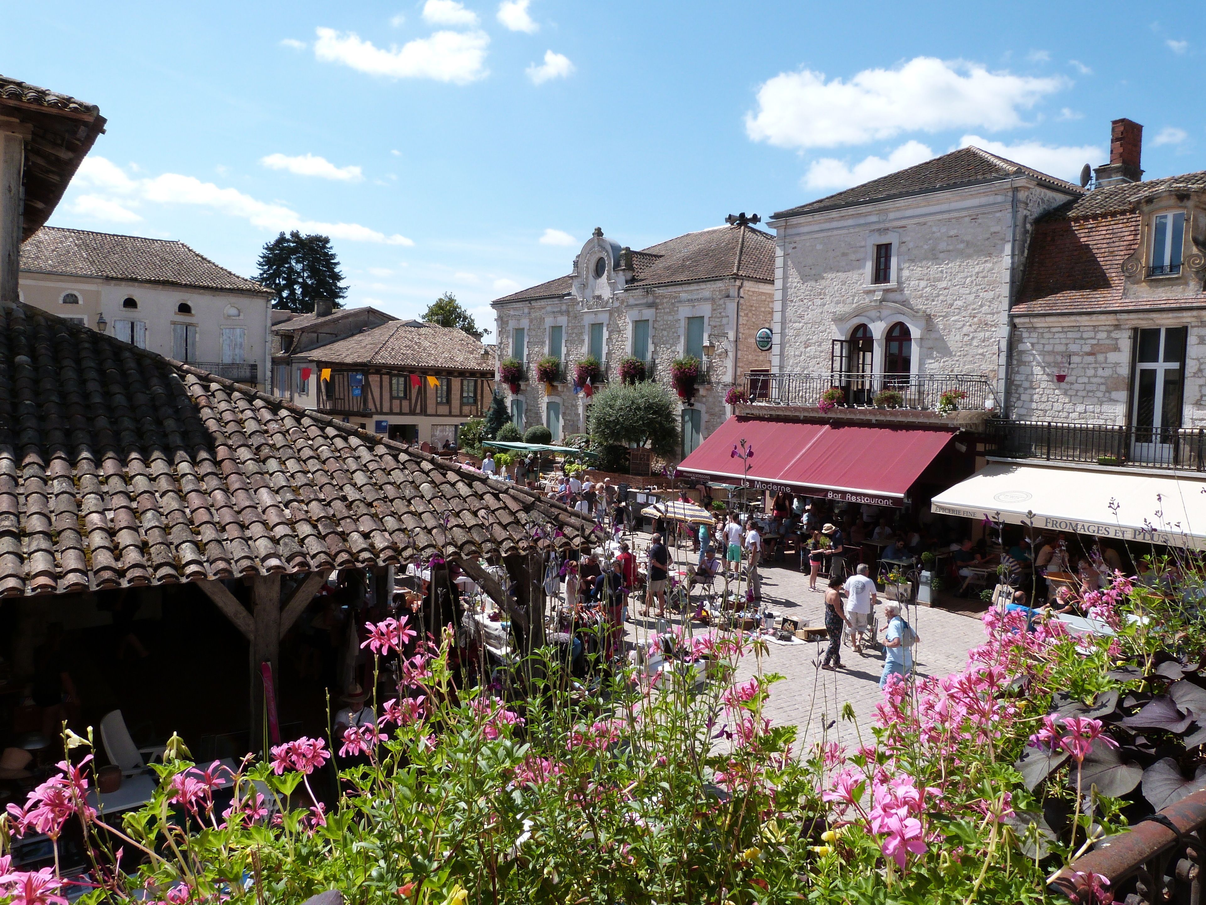 Un mercado al aire libre animado con edificios de piedra, una zona de estar cubierta y flores coloridas.