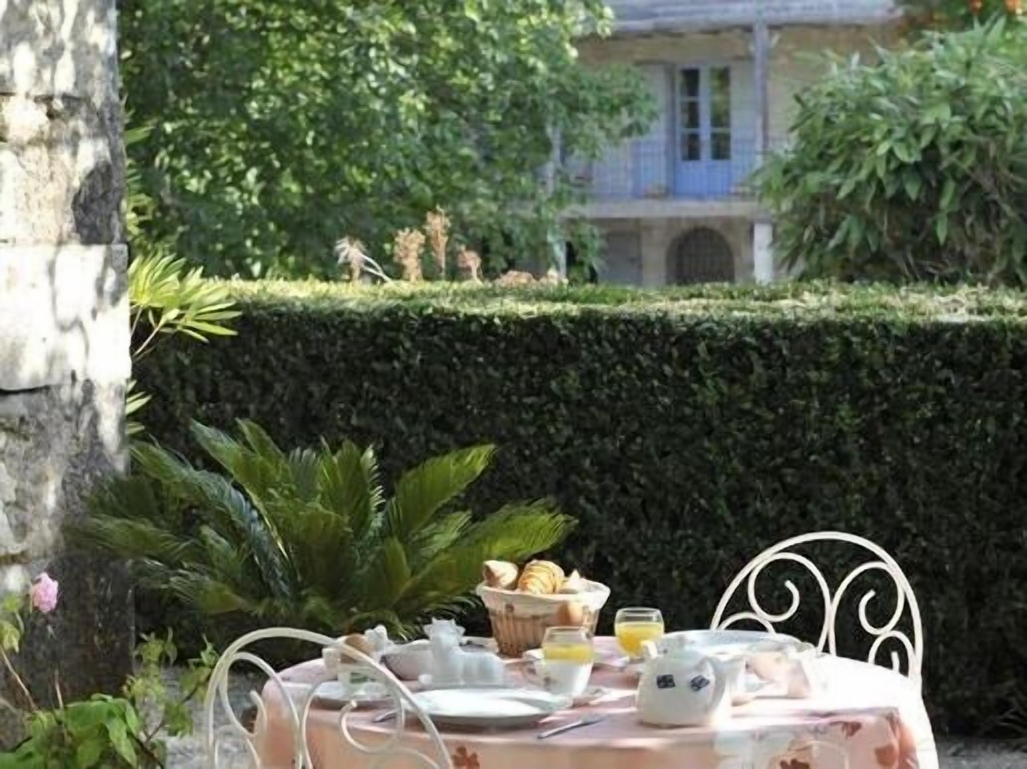 Une table dressée à l’extérieur avec des aliments pour le petit-déjeuner, une chaise en métal et une haie en arrière-plan.