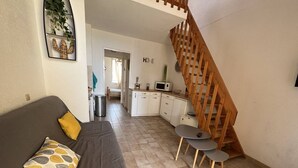A living room with a sofa, a small table, and a wooden staircase. - T2 + Mezzanine, 6 pers, Terrace, BBQ, Close to the beach (Port Barcarès)