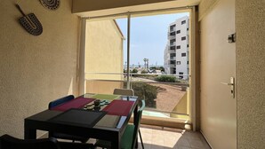 A balcony with a table and chairs, a view of a building, and a door. - T2 + Mezzanine, 6 pers, Terrace, BBQ, Close to the beach (Port Barcarès)