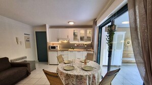 Un espace de vie compact comprenant un coin repas, une kitchenette et une porte-fenêtre coulissante donnant sur un balcon.