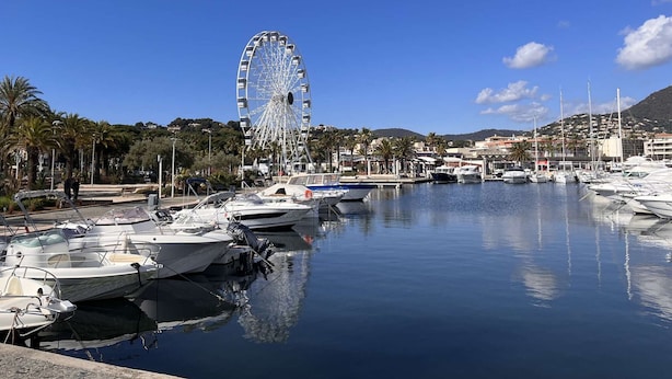 Un port de plaisance avec des bateaux amarrés, une grande roue et une ville côtière en arrière-plan.