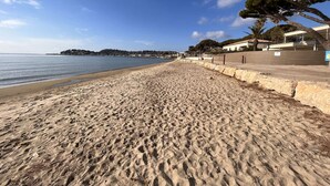 Une plage de sable bordée d’un mur de pierres, avec une rangée de bâtiments en arrière-plan.