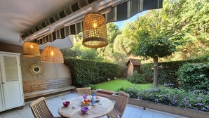 Une terrasse extérieure avec une table ronde en bois, quatre chaises en bois et des lampes en osier suspendues.