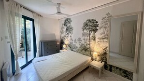 Une chambre à coucher comprenant un lit, une commode, un ventilateur de plafond, une fenêtre avec des rideaux et une fresque murale.