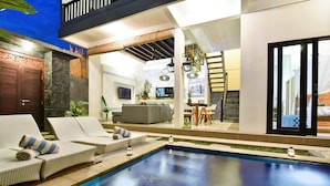 Uma área de piscina moderna com espreguiçadeiras, uma piscina pequena e um espaço de estar com sofá e mesa de jantar.