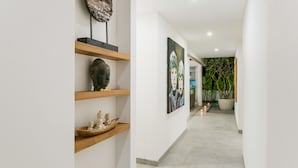 Um corredor com paredes brancas, prateleiras de madeira exibindo esculturas e um quadro grande.