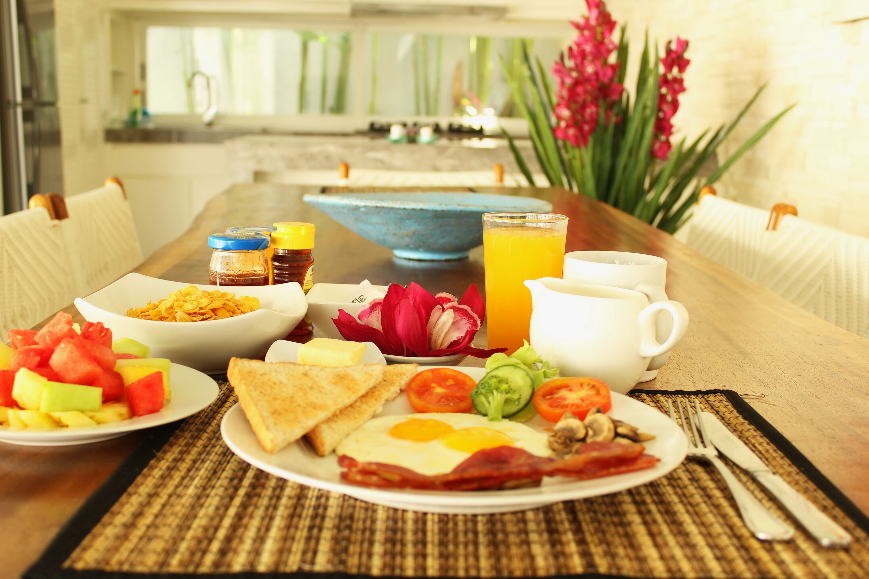 A breakfast setting with a variety of dishes including toast, eggs, bacon, tomatoes, cucumbers, and a fruit salad.