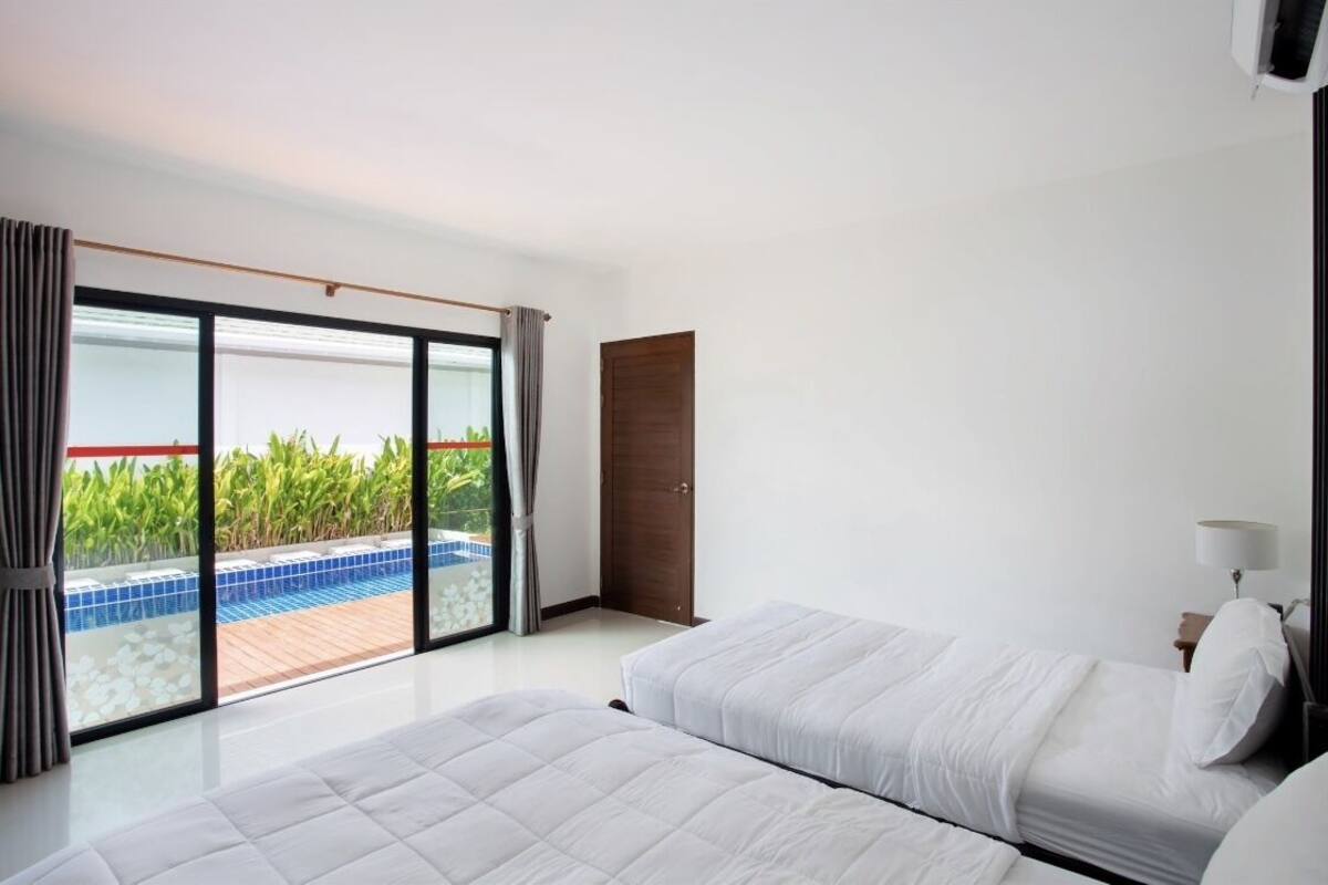 A hotel room with two beds, a sliding glass door to a pool area, and a wooden door.