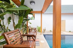 A poolside area with wooden benches and lush tropical plants. - Sanga Villas (Rawai)