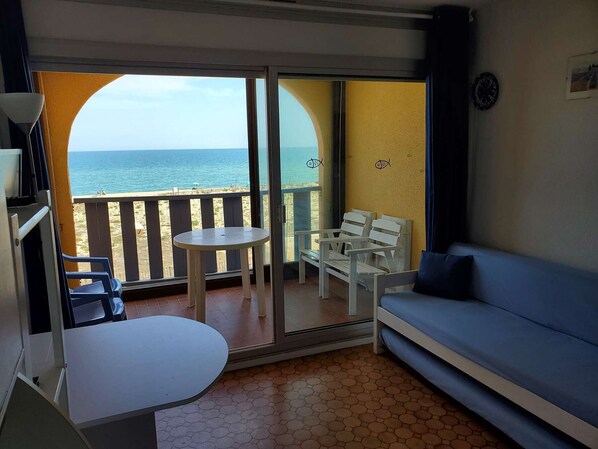 A balcony with a view of the sea, a white sofa, and a small table.