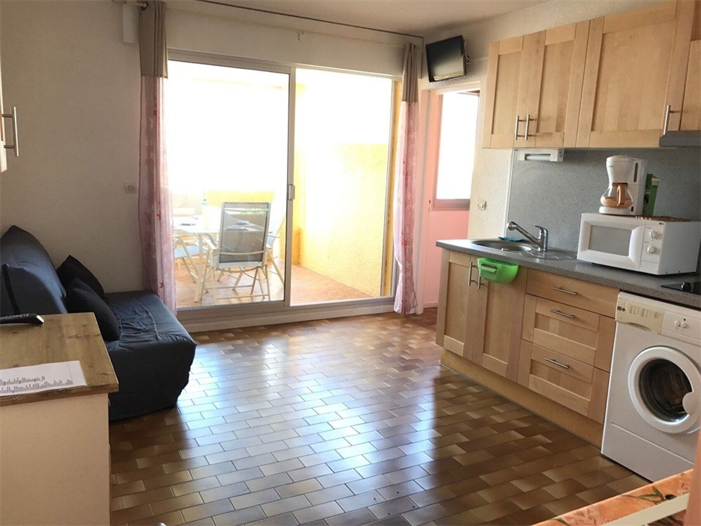 A compact living space with a sofa, a washing machine, a microwave, and a small dining area with a table and chairs.