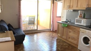 Un espace de vie compact comprenant un canapé, un lave-linge, un four à micro-ondes et un petit coin repas avec une table et des chaises.