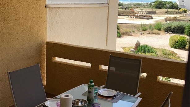 Un balcon avec une table dressée pour deux personnes, des chaises, une bouteille et une vue sur la plage et l’océan.