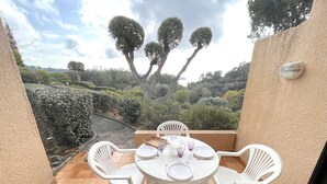 Eine Terrasse mit rundem Tisch und vier Stühlen, umgeben von einer beigen Mauer und Blick auf einen angelegten Garten mit Bäumen und Sträuchern.