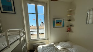 Une chambre de dortoir avec des lits superposés, une fenêtre donnant sur des immeubles et un tableau encadré accroché au mur.