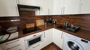 Une cuisine moderne avec des meubles blancs, un pare-feu en bois, un four encastré, un four à micro-ondes, un évier et un lave-linge.
